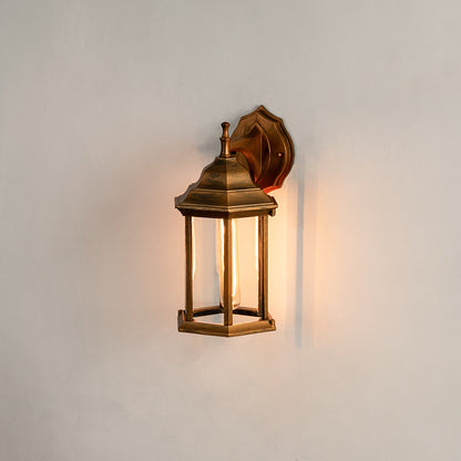 Antique brass outdoor wall light on white background featuring a clear glass lantern frame for minimal entry path decor.