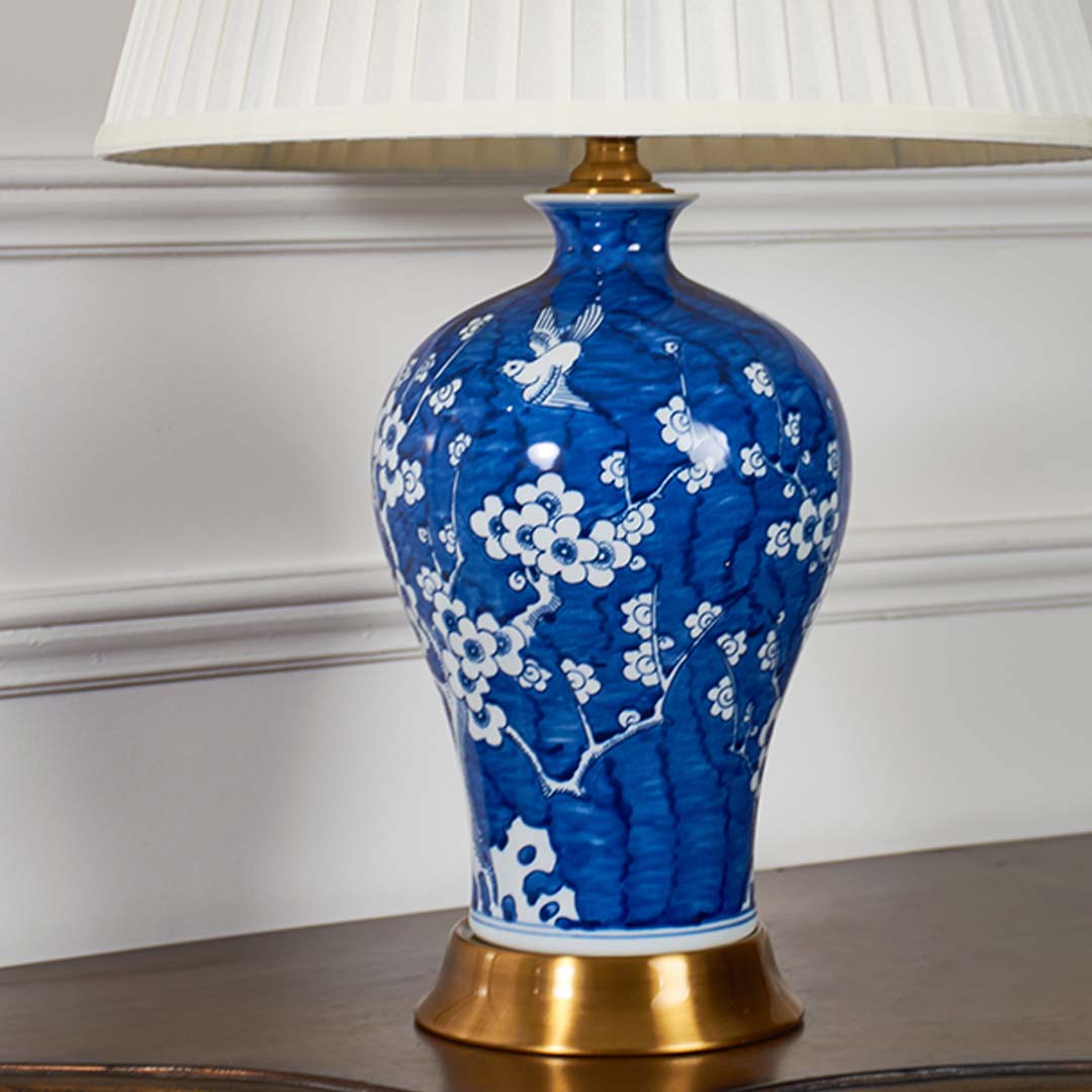 Closeup of blue ceramic table lamp with intricate white floral detailing and cream pleated shade showcasing premium classic craftsmanship.