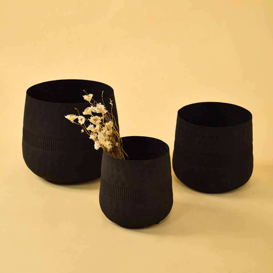 Trio of matte black textured artisan metal vases for contemporary home decor and stylish interior shelf display needs.