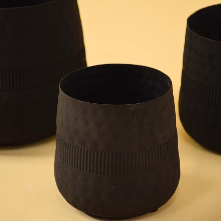 Closeup of small black textured pot shown with other pots highlighting rich surface texture and matte black interior.