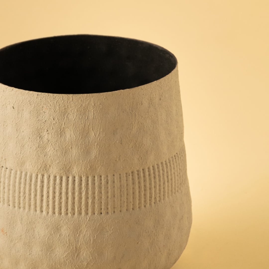 Closeup of small cream textured pot showing detailed ribbed pattern and matte black interior for modern stylish decor.