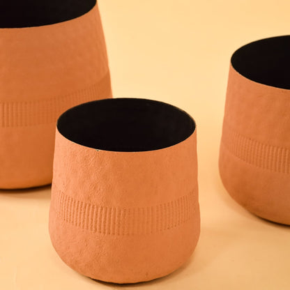 Closeup of terracotta textured pot shown with other pots highlighting rich surface texture and matte black interior.
