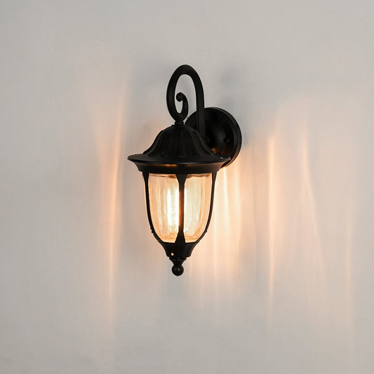 Black metal outdoor wall light on white background with clear glass shade casting a warm radial glow for balcony decor.