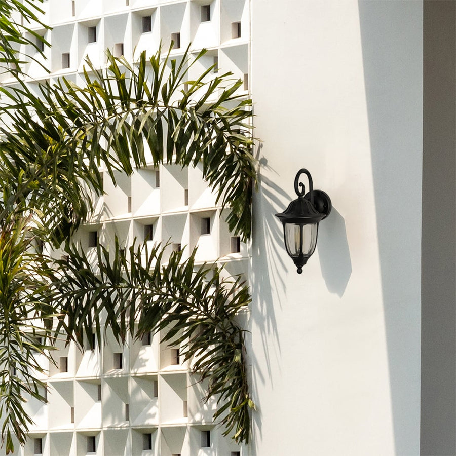 Elegant black metal outdoor wall light fixture mounted on a modern white patio wall beside tropical plants.