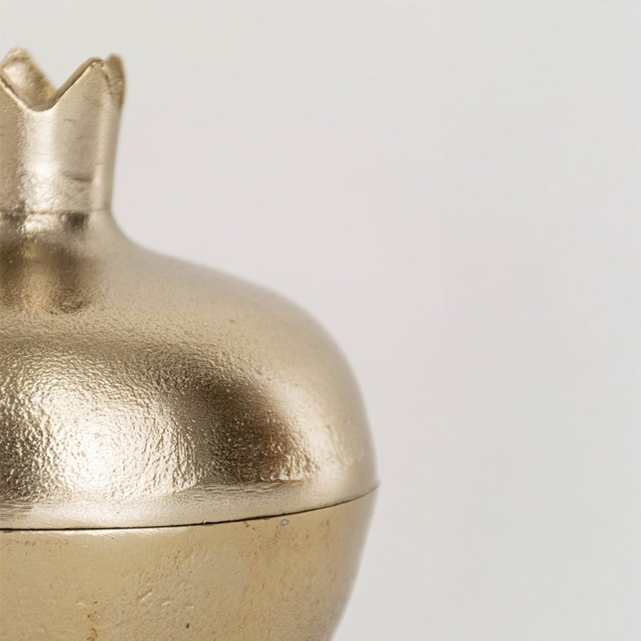Close view of gold pomegranate storage jar highlighting smooth metallic finish and sculpted crown lid detail