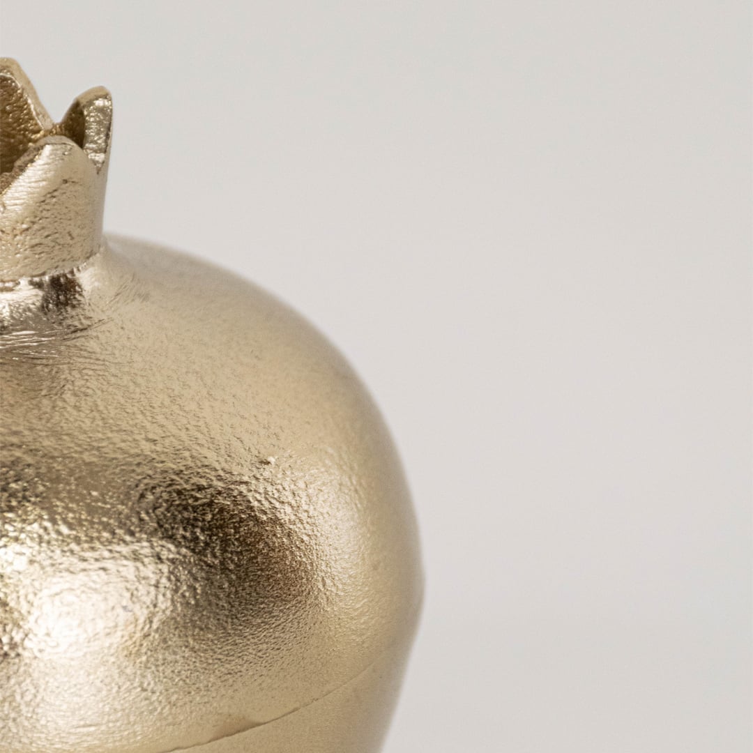 Close view of small gold pomegranate container showing smooth metallic finish and sculpted crown lid detail