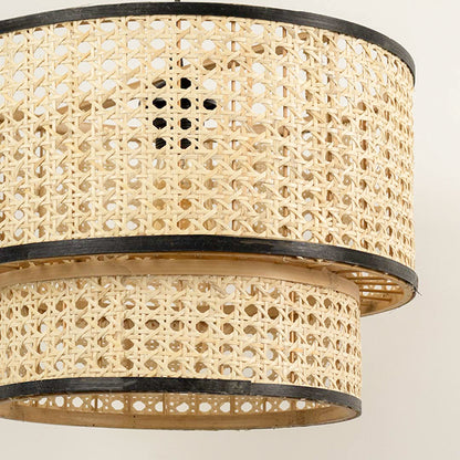 Layered cane pendant light with double drum design and black metal frame detail hanging against clean neutral wall background for contemporary decor.