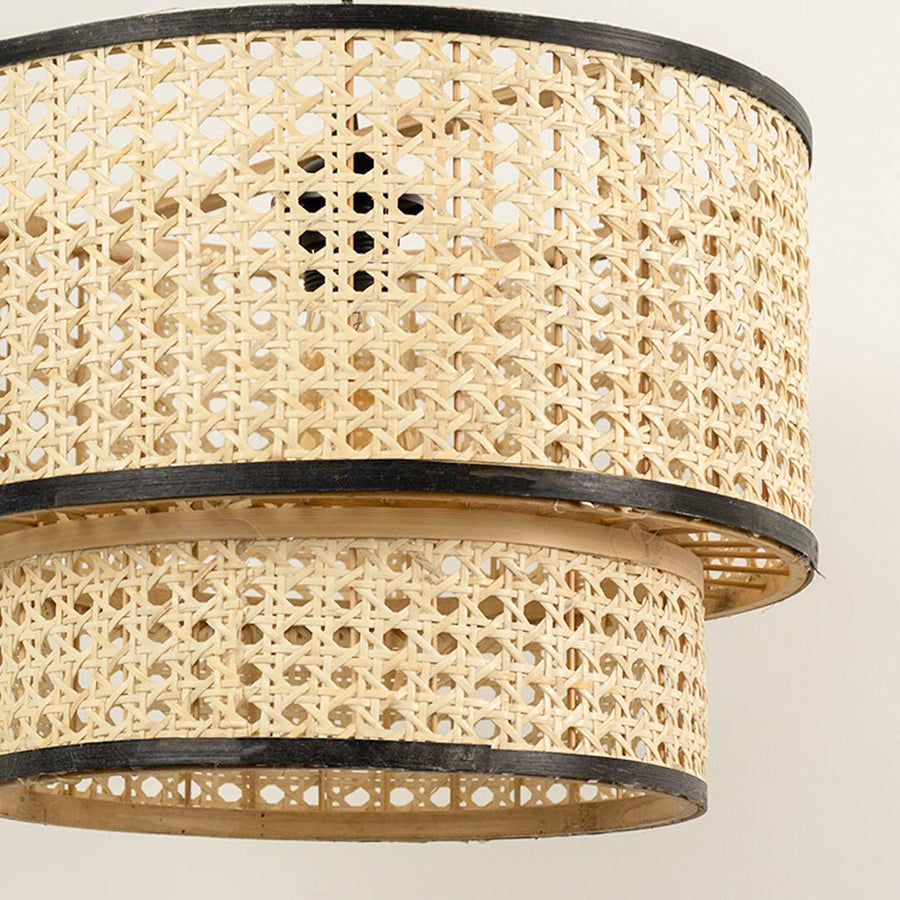 Layered cane pendant light with double drum design and black metal frame detail hanging against clean neutral wall background for contemporary decor.