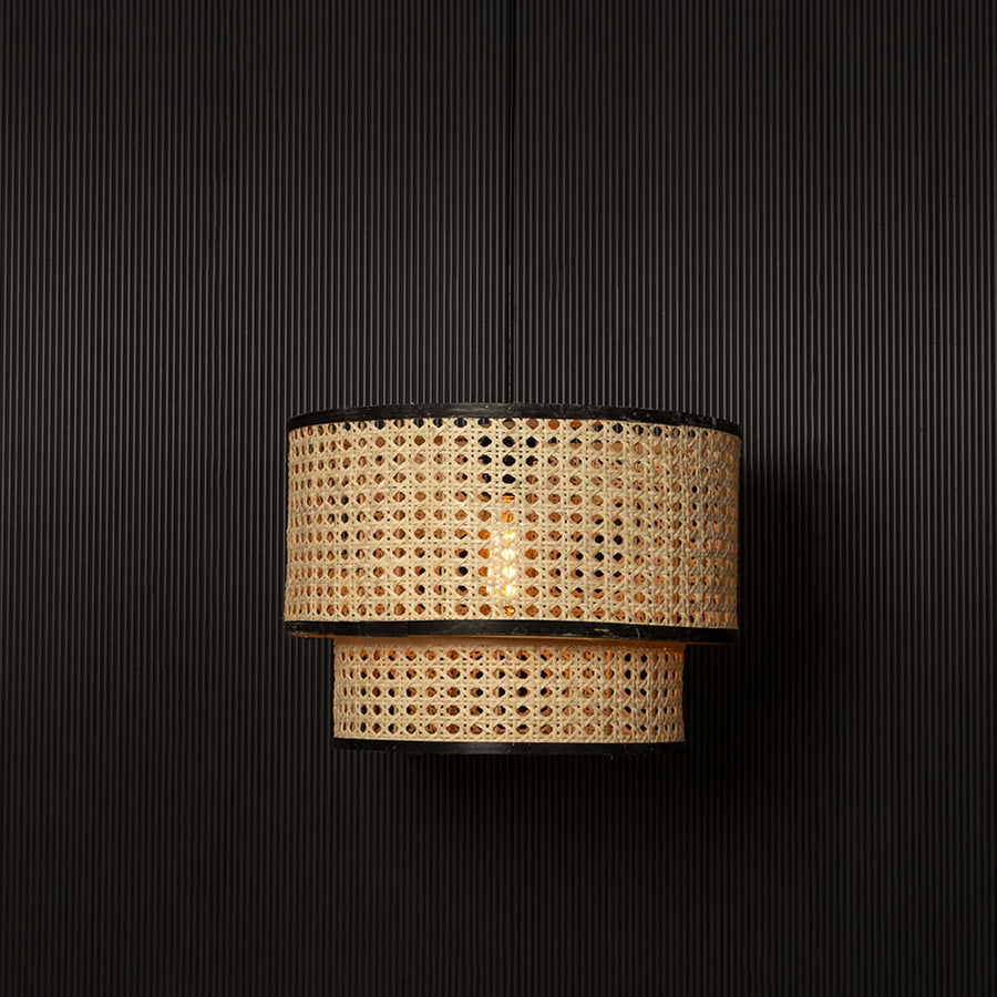 Natural cane hanging light glowing softly through woven pattern creating warm ambience on black background.