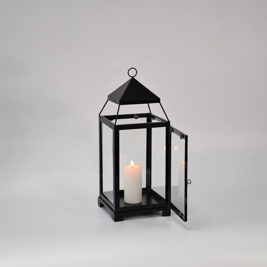 Black metal glass lantern with candle lit shown on white background highlighting warm glow classic frame design and home decor use.