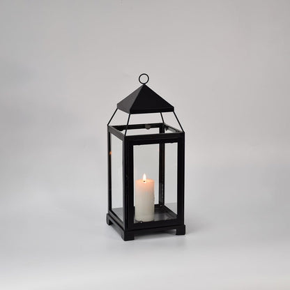 Black metal glass lantern with candle lit shown on white background highlighting warm glow classic frame design and home decor use.