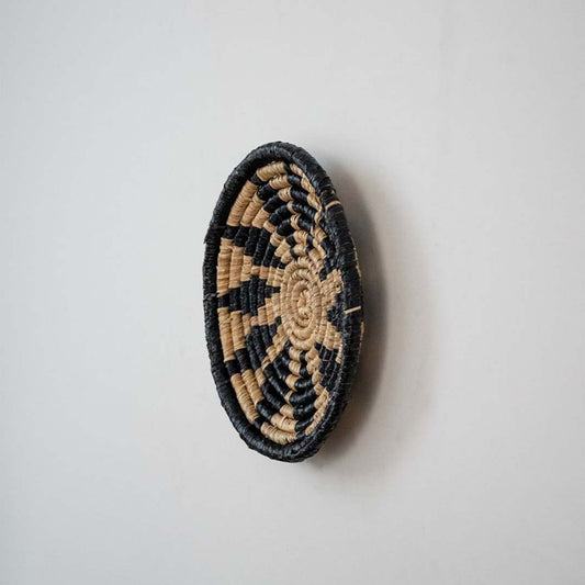 Handwoven wicker wall decor plate side view in beige and black spiral weave natural fiber showing texture and thickness.