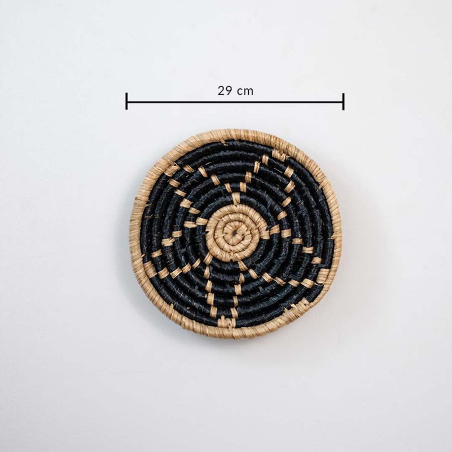 Handwoven wicker wall decor plate 29 cm round in beige and black natural fiber light off white background with size shown.