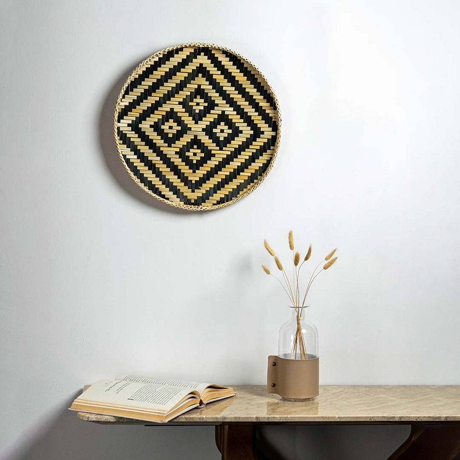 Black and natural woven bamboo basket with tribal diamond pattern displayed as bohemian handcrafted wall decor accent.