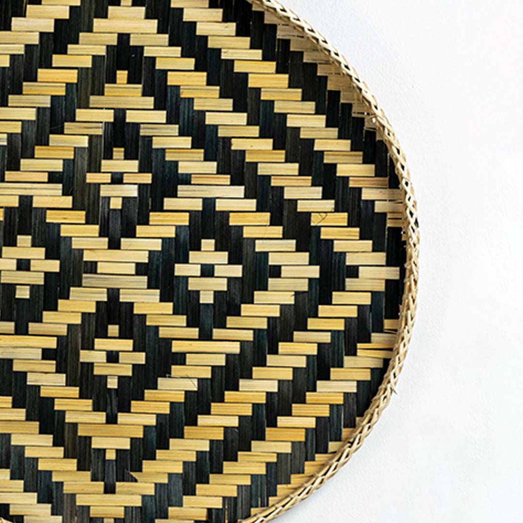 Closeup of handwoven wall basket edge with black and gold geometric weave highlighting natural fiber texture and artisan craftsmanship.
