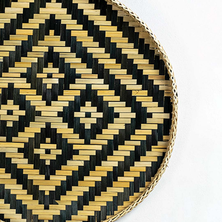 Closeup of handwoven wall basket edge with black and gold geometric weave highlighting natural fiber texture and artisan craftsmanship.