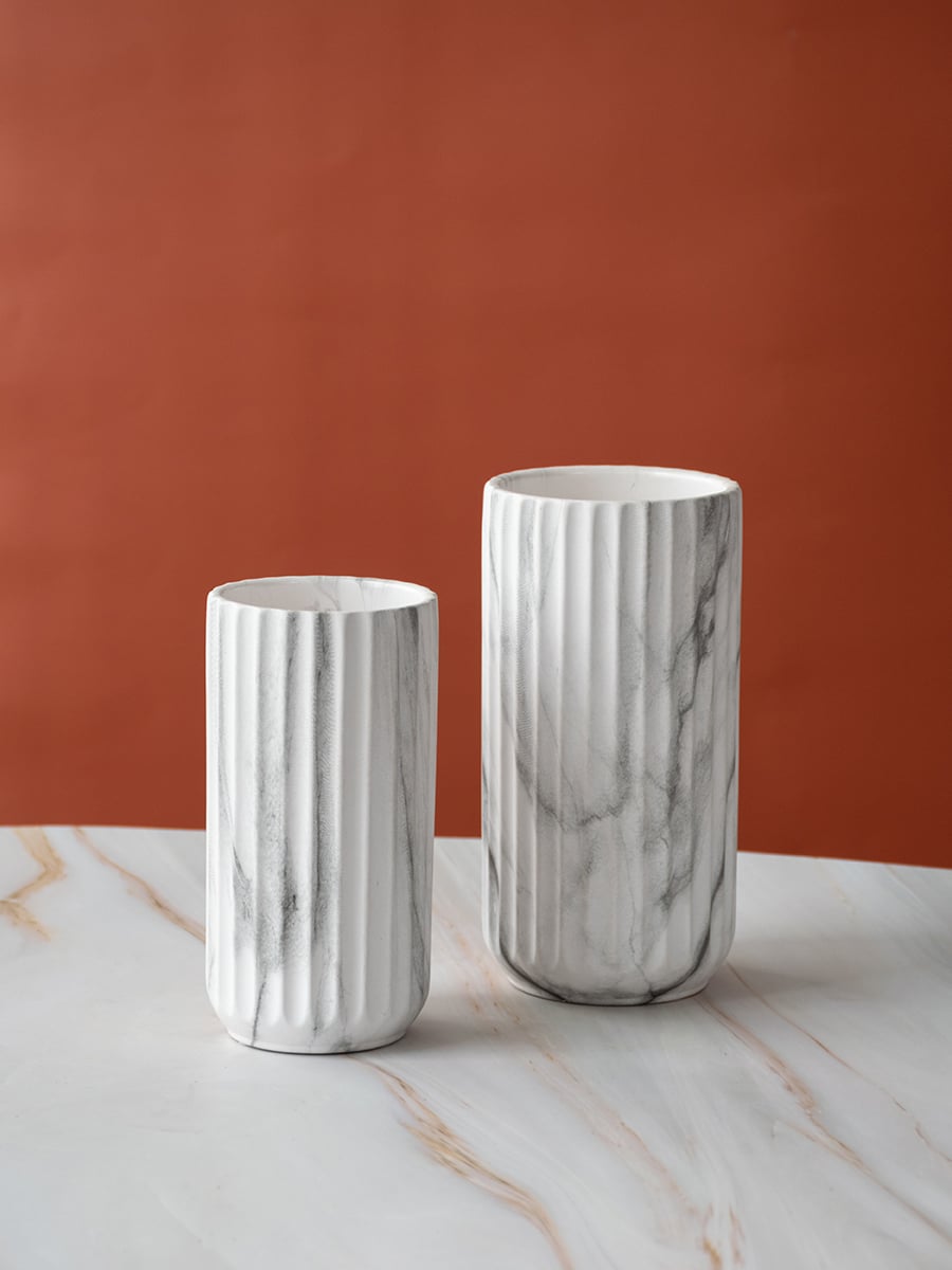 A marble textured cylindrical vase displayed as part of a decor set showing its vertical grooves and elegant stone inspired finish in a clean setup.