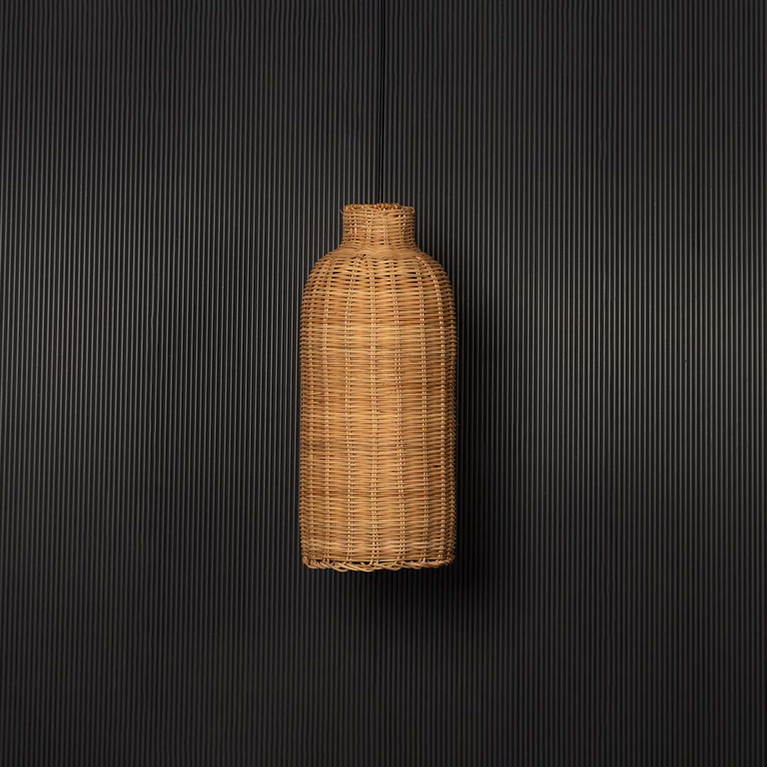 Rattan pendant light bulb off on black background with tall bottle shaped wicker shade for rustic bohemian lighting.