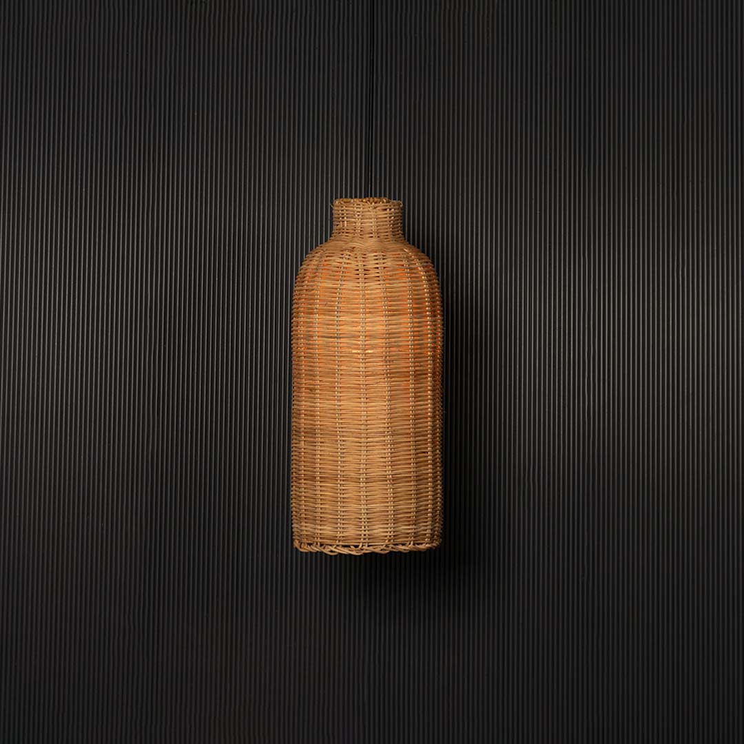 Woven rattan pendant light glowing on black background with tall cylindrical bottle shaped wicker shade design.