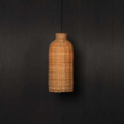 Woven rattan pendant light glowing on black background with tall cylindrical bottle shaped wicker shade design.