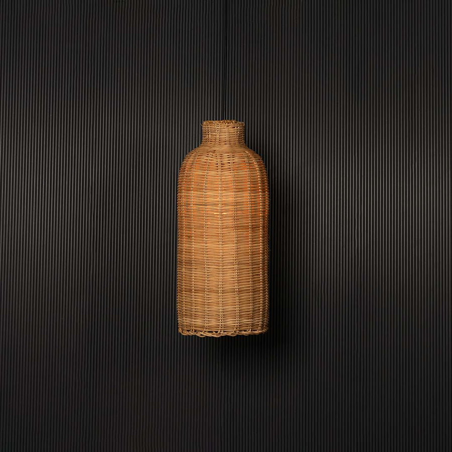 Woven rattan pendant light glowing on black background with tall cylindrical bottle shaped wicker shade design.