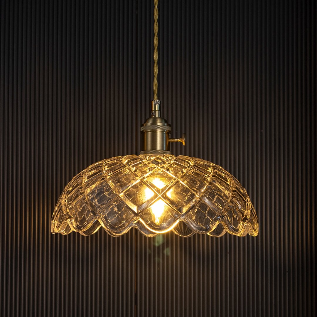 Crystal glass pendant light with golden glow against dark background highlighting intricate diamond cut glass pattern.