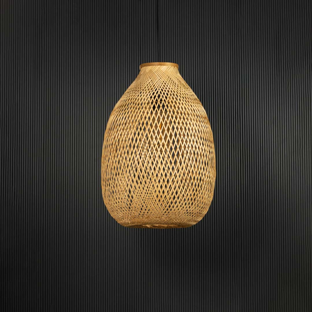 Rattan pendant light with tall handwoven bamboo shade in natural finish turned off against black background.