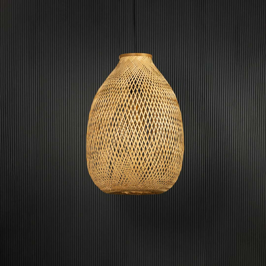 Rattan pendant light with tall handwoven bamboo shade in natural finish turned off against black background.