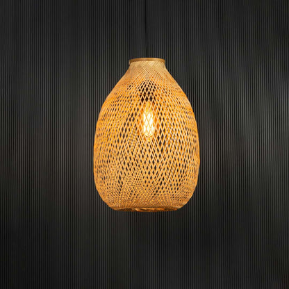 Handwoven rattan pendant light with tall bamboo shade turned on glowing softly against black background.