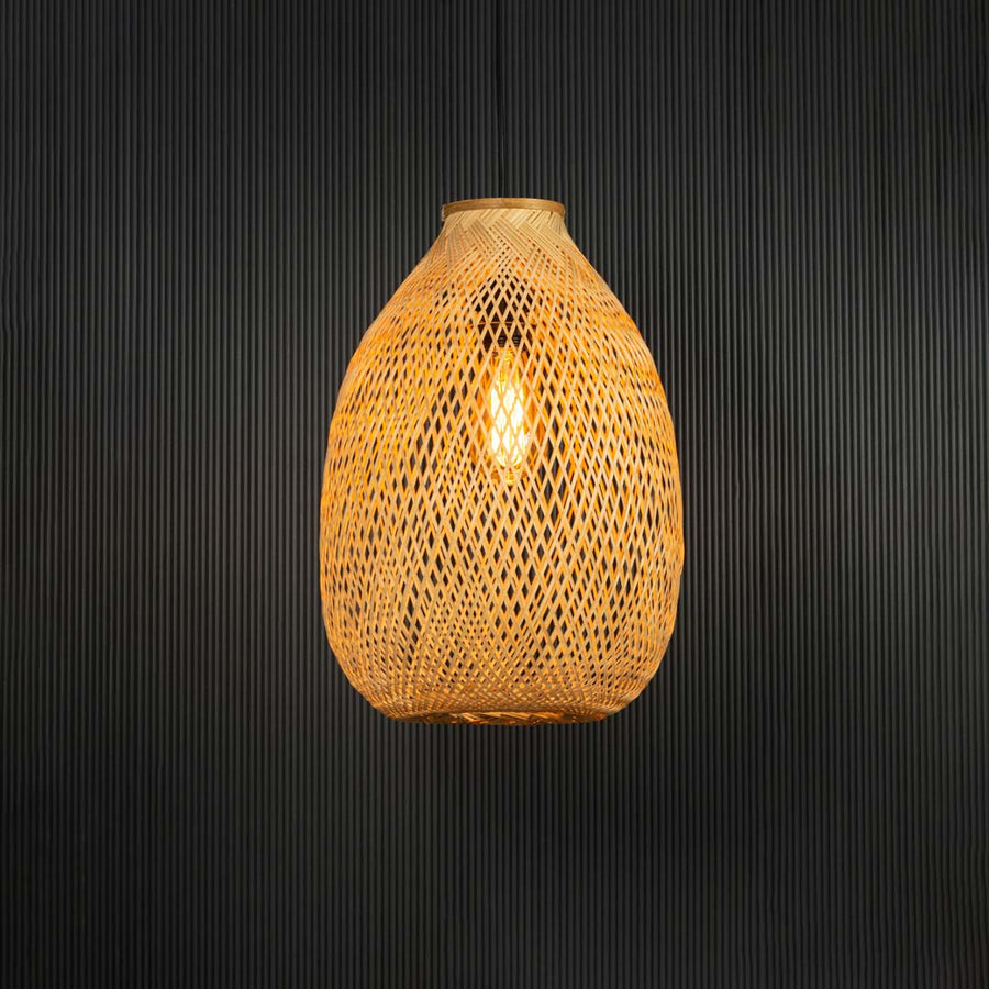 Handwoven rattan pendant light with tall bamboo shade turned on glowing softly against black background.
