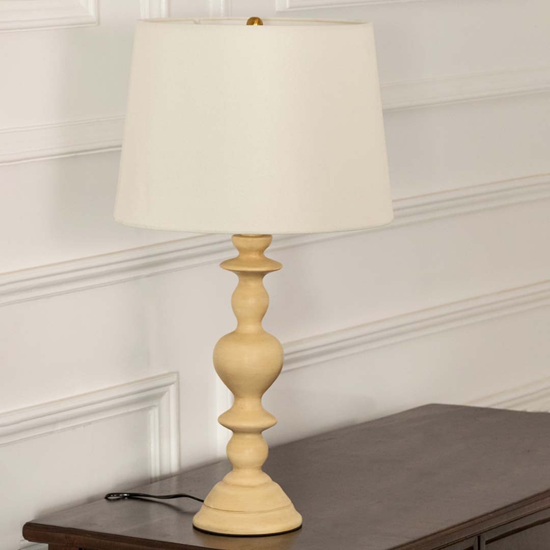 White shade beige spindle base table lamp on wooden sideboard with light off for warm traditional décor.