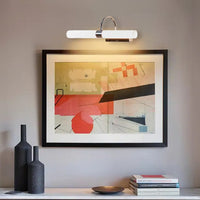 White and chrome picture light illuminating framed artwork in a modern living room creating warm focused lighting for elegant wall decor.