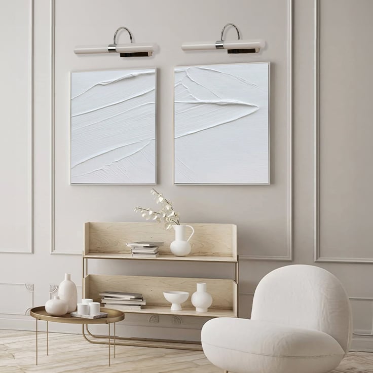 White and chrome picture light highlighting framed art creating warm focused illumination for modern home and hallway wall decor.