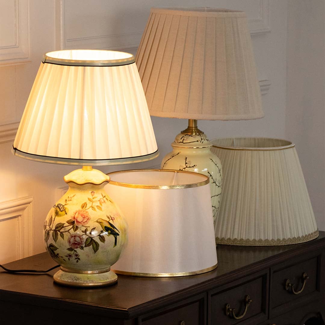 Table lamps light on with floral bases and pleated white shades placed on a wooden console creating a warm elegant ambience.