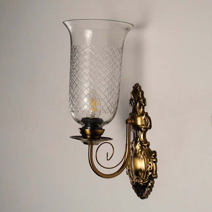 Vintage style gold wall light fixture with etched glass cylinder turned off isolated on a plain white background.