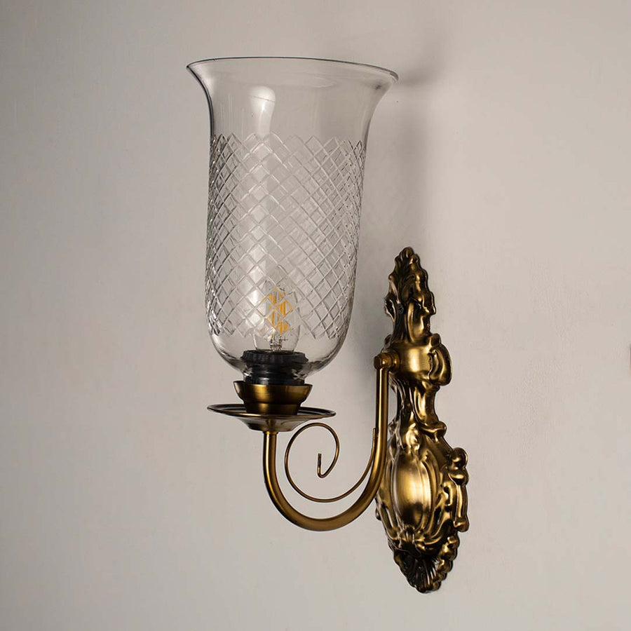 Vintage style gold wall light fixture with etched glass cylinder turned off isolated on a plain white background.