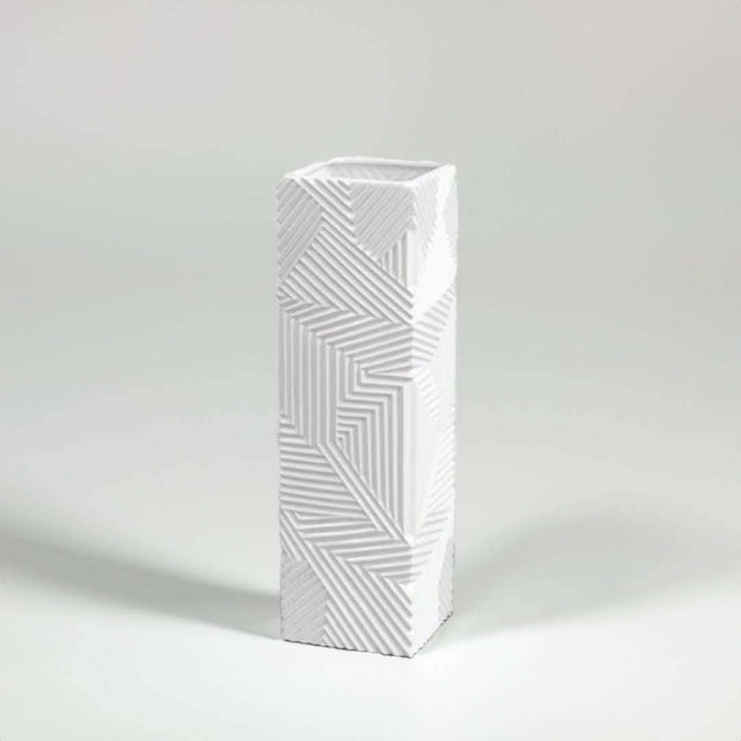 Tall white geometric ceramic vase with raised linear texture photographed on a white background highlighting its sharp modern design.