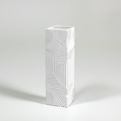Tall white geometric ceramic vase with raised linear texture photographed on a white background highlighting its sharp modern design.