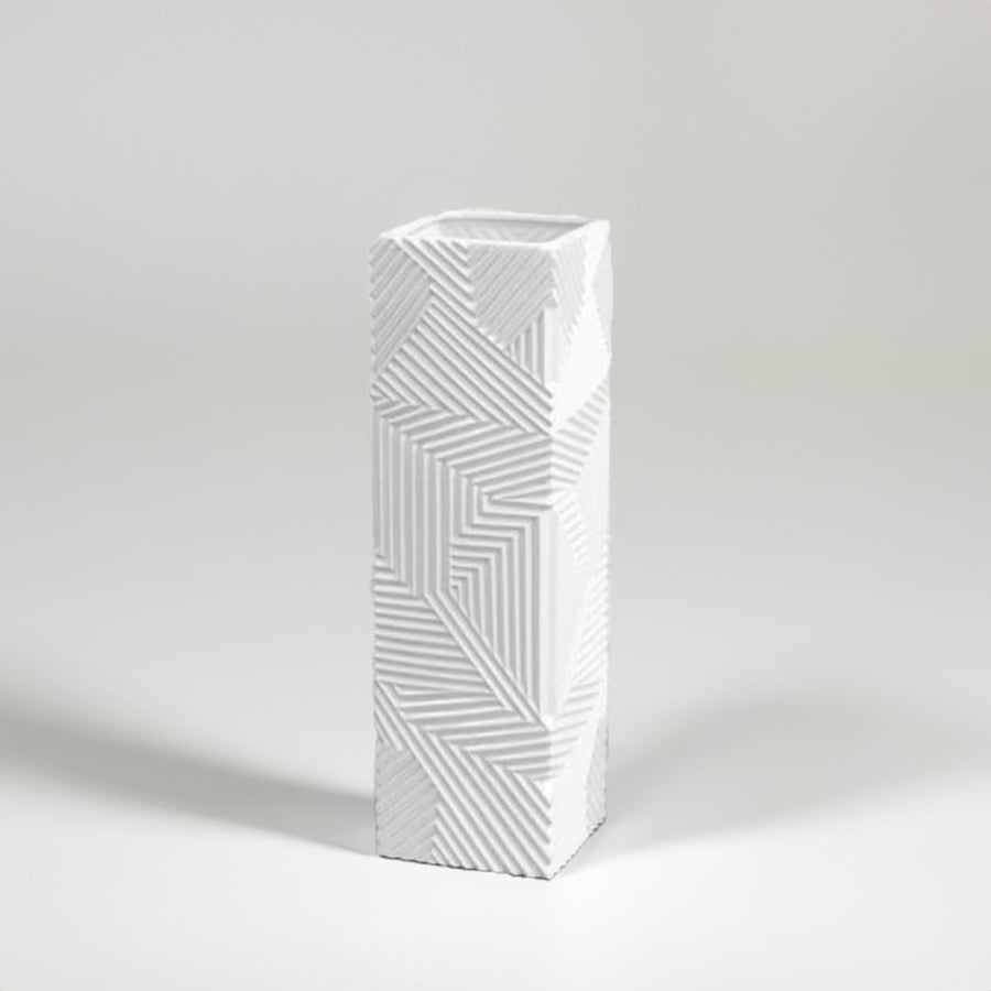 Tall white geometric ceramic vase with raised linear texture photographed on a white background highlighting its sharp modern design.