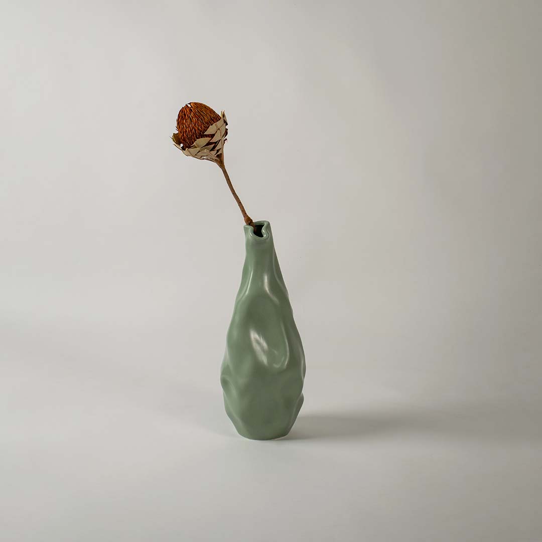 A modern green sculpted vase displayed in a soft lifestyle setting showing its unique organic shape and smooth artistic texture that enhances any contemporary decor.