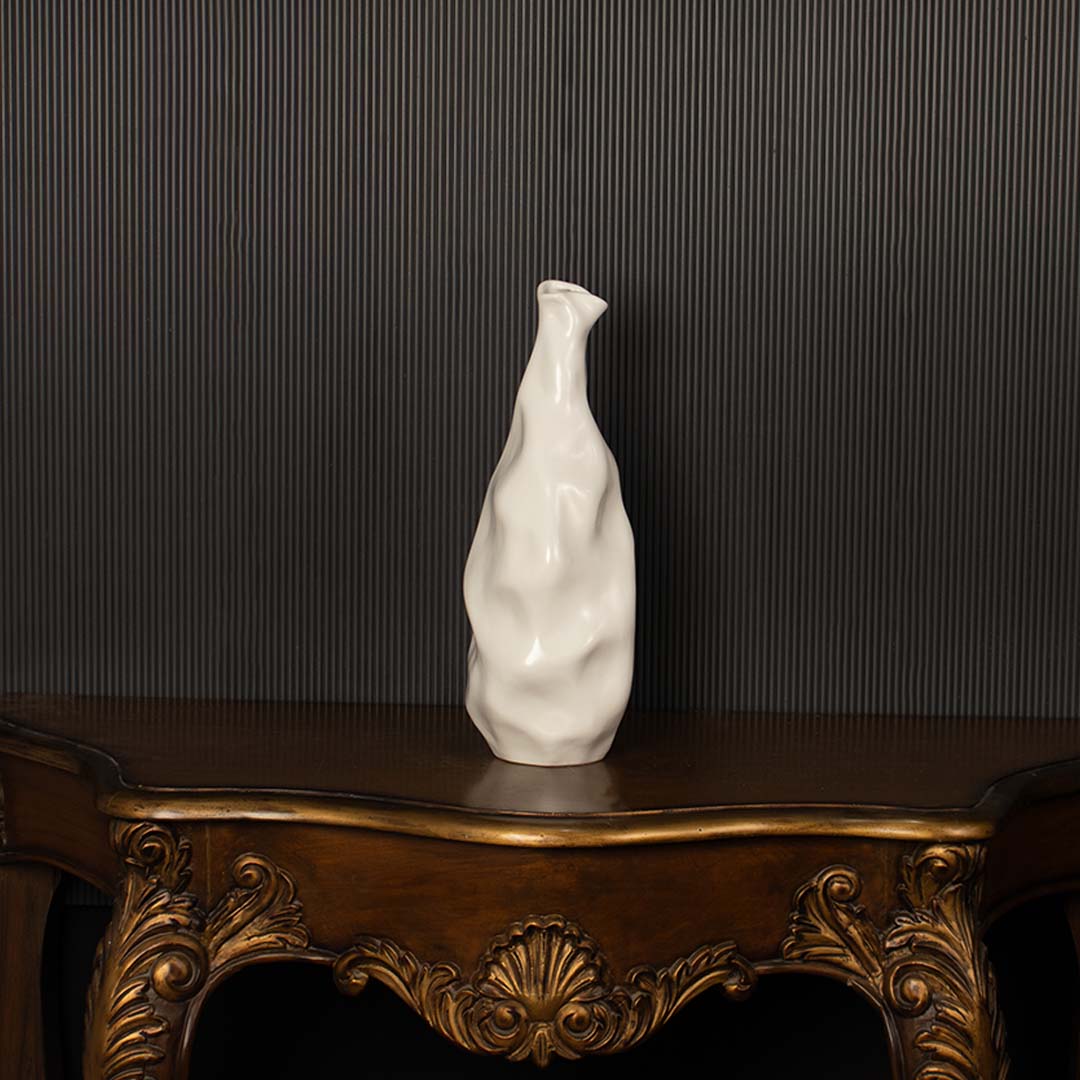 A sculpted white ceramic vase highlighted against a dark black background  showcasing its tall artistic shape with refined sculpted details.