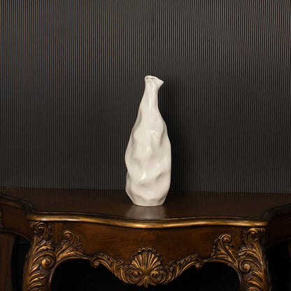 A sculpted white ceramic vase highlighted against a dark black background  showcasing its tall artistic shape with refined sculpted details.