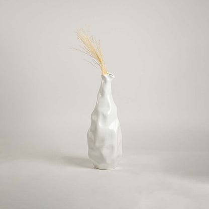 A modern sculpted white ceramic vase placed on a soft white backdrop  focusing on its tall organic silhouette and elegant handcrafted style.