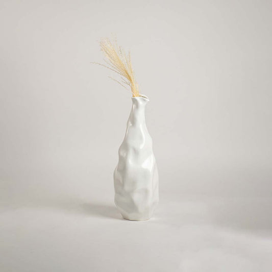 A modern sculpted white ceramic vase placed on a soft white backdrop  focusing on its tall organic silhouette and elegant handcrafted style.