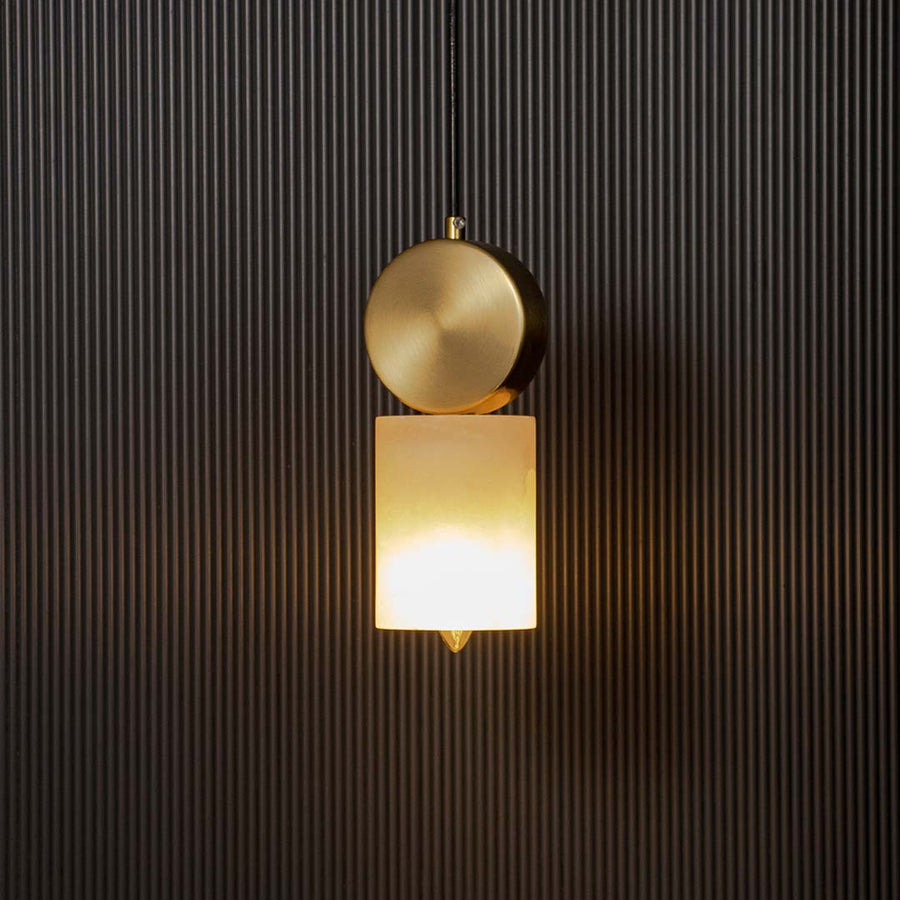 Elegant gold pendant light with frosted cylindrical glass shade glowing warmly on black background for luxury home lighting.