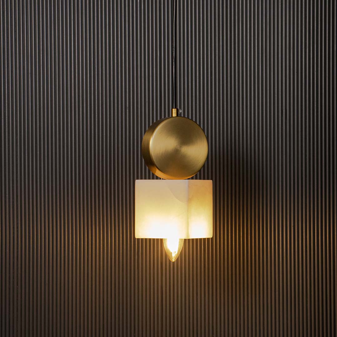 Modern brass pendant lamp with frosted cube glass shade glowing warmly on black background for home interiors.