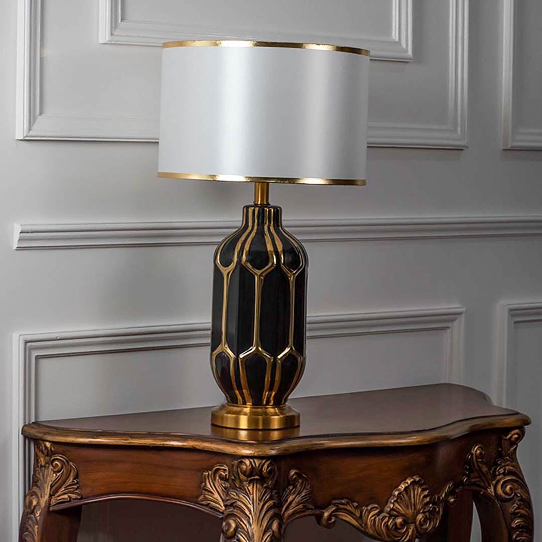 Black gold ceramic lamp with white shade switched off on plain white background.