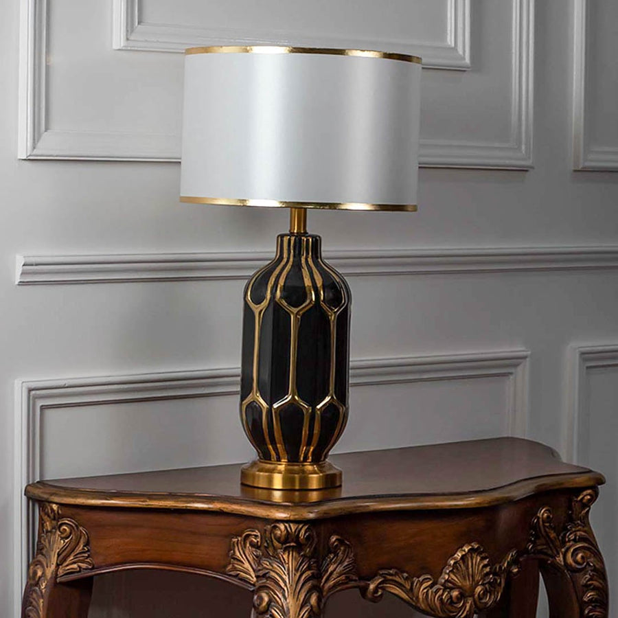 Black gold ceramic lamp with white shade switched off on plain white background.