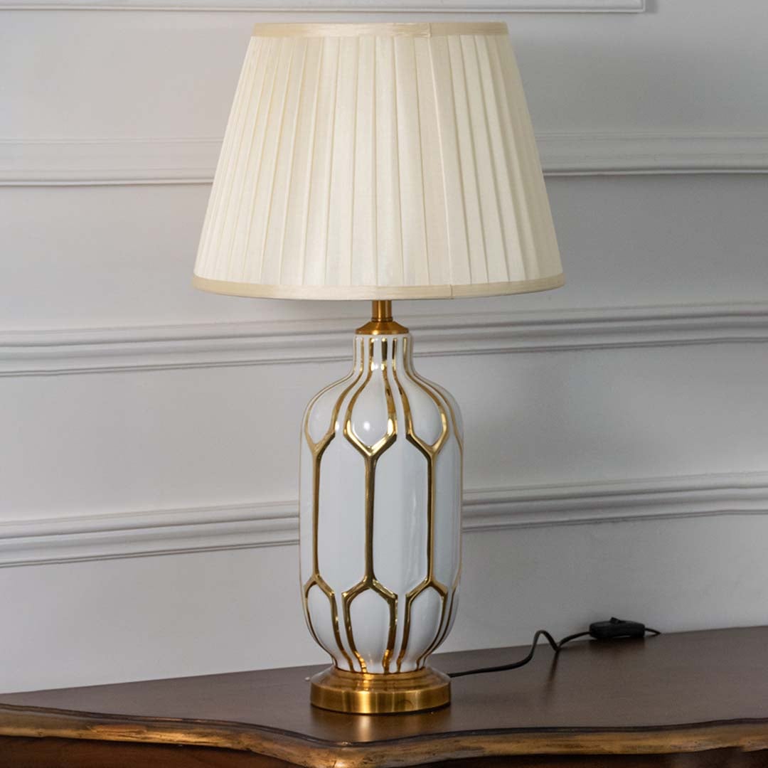 Modern white ceramic table lamp with geometric gold detailing and pleated beige shade turned off on white background showcasing luxury craftsmanship.
