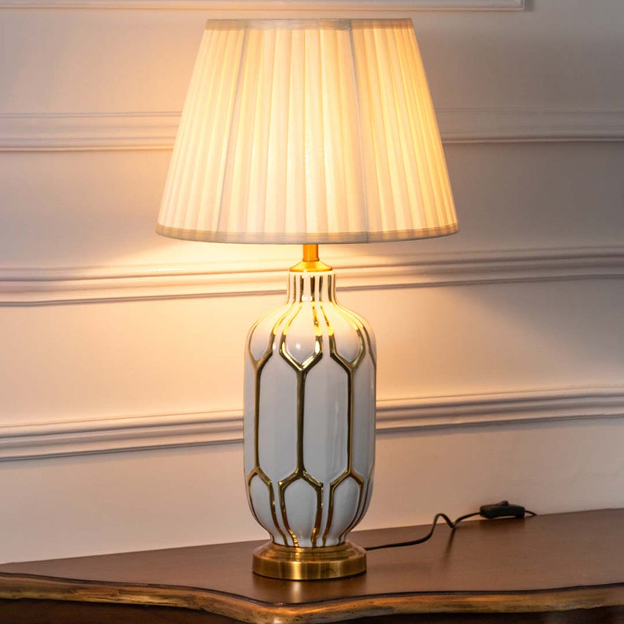 White geometric ceramic table lamp with pleated fabric shade creating warm modern ambient lighting on a console table.